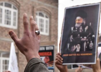 Des manifestants lèvent les mains en brandissant une affiche de Khamenei, exprimant leur désaccord en plein air.