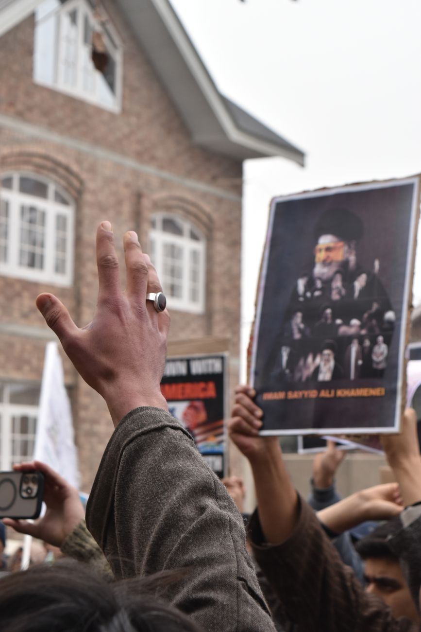 Des manifestants lèvent les mains en brandissant une affiche de Khamenei, exprimant leur désaccord en plein air.