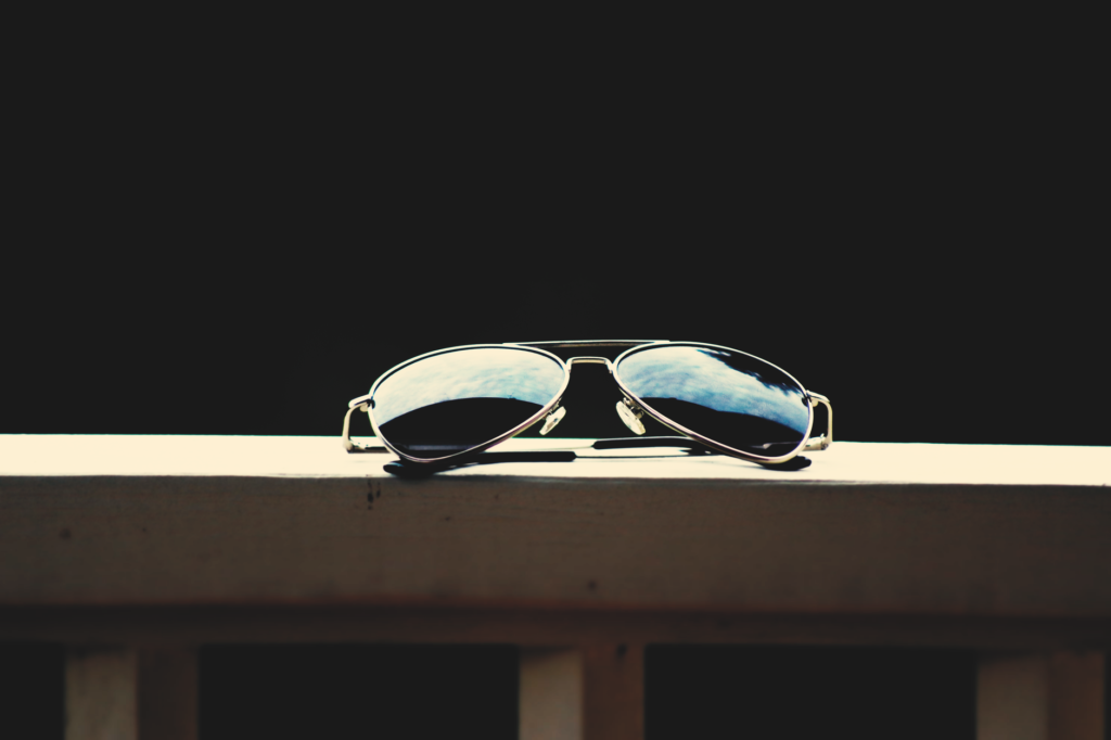 Un gros plan de lunettes de soleil aviateur reflétant le ciel, sur fond sombre.