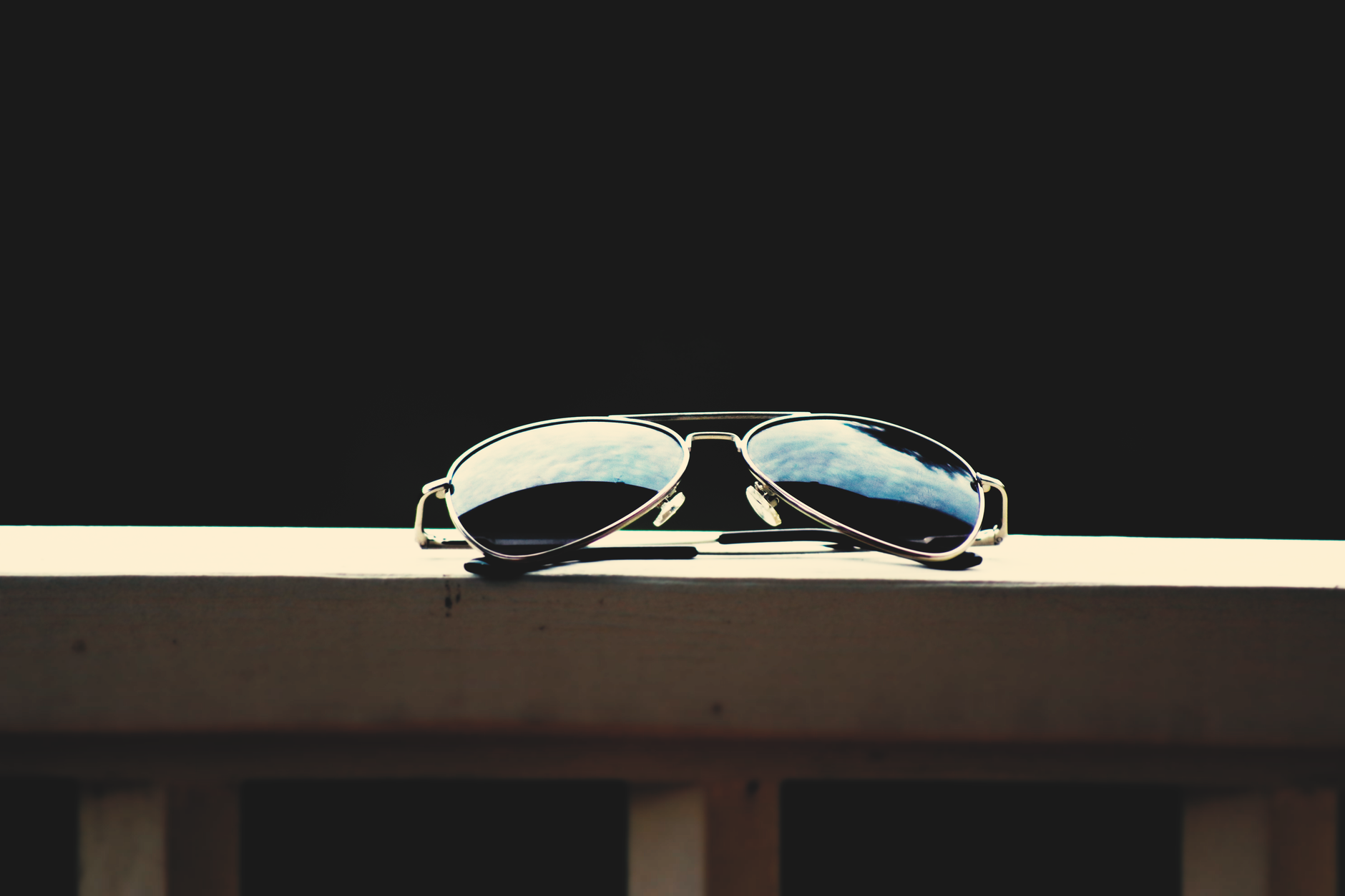 Un gros plan de lunettes de soleil aviateur reflétant le ciel, sur fond sombre.
