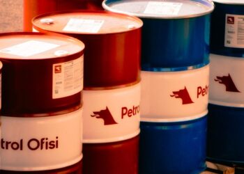 Une collection de barils de pétrole rouges et bleus étiquetés 'Ofisi de Pétrole' dans un cadre industriel en plein air en Turquie.