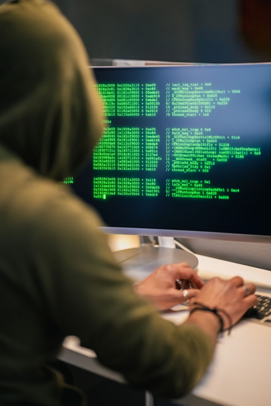 Personne portant un hoodie tapant du code sur un écran d'ordinateur avec du texte vert, représentant une scène de hacking.
