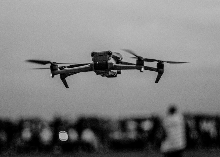 Une image en noir et blanc d'un drone survolant une foule à l'extérieur, mettant en valeur la technologie en vol.