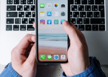 Vue rapprochée de mains tenant un smartphone avec des applications sur un clavier d'ordinateur portable.