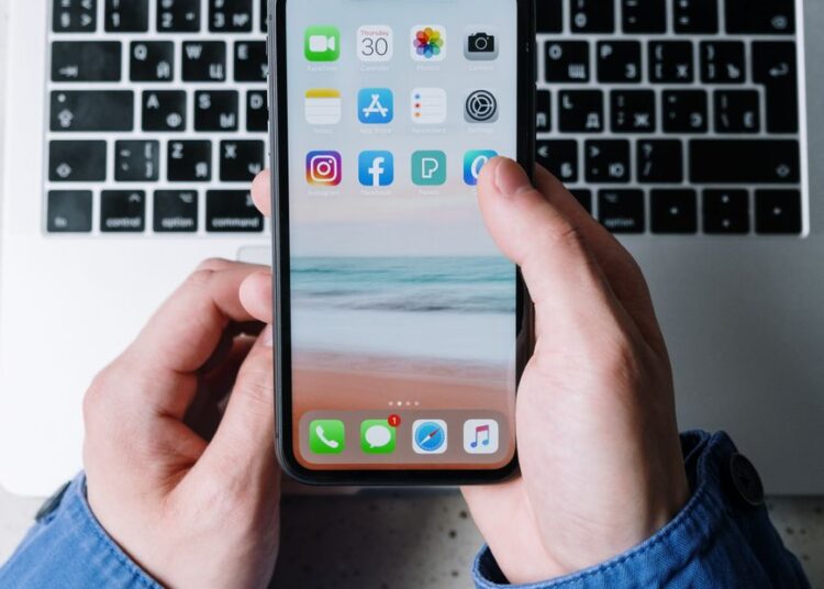 Vue rapprochée de mains tenant un smartphone avec des applications sur un clavier d'ordinateur portable.