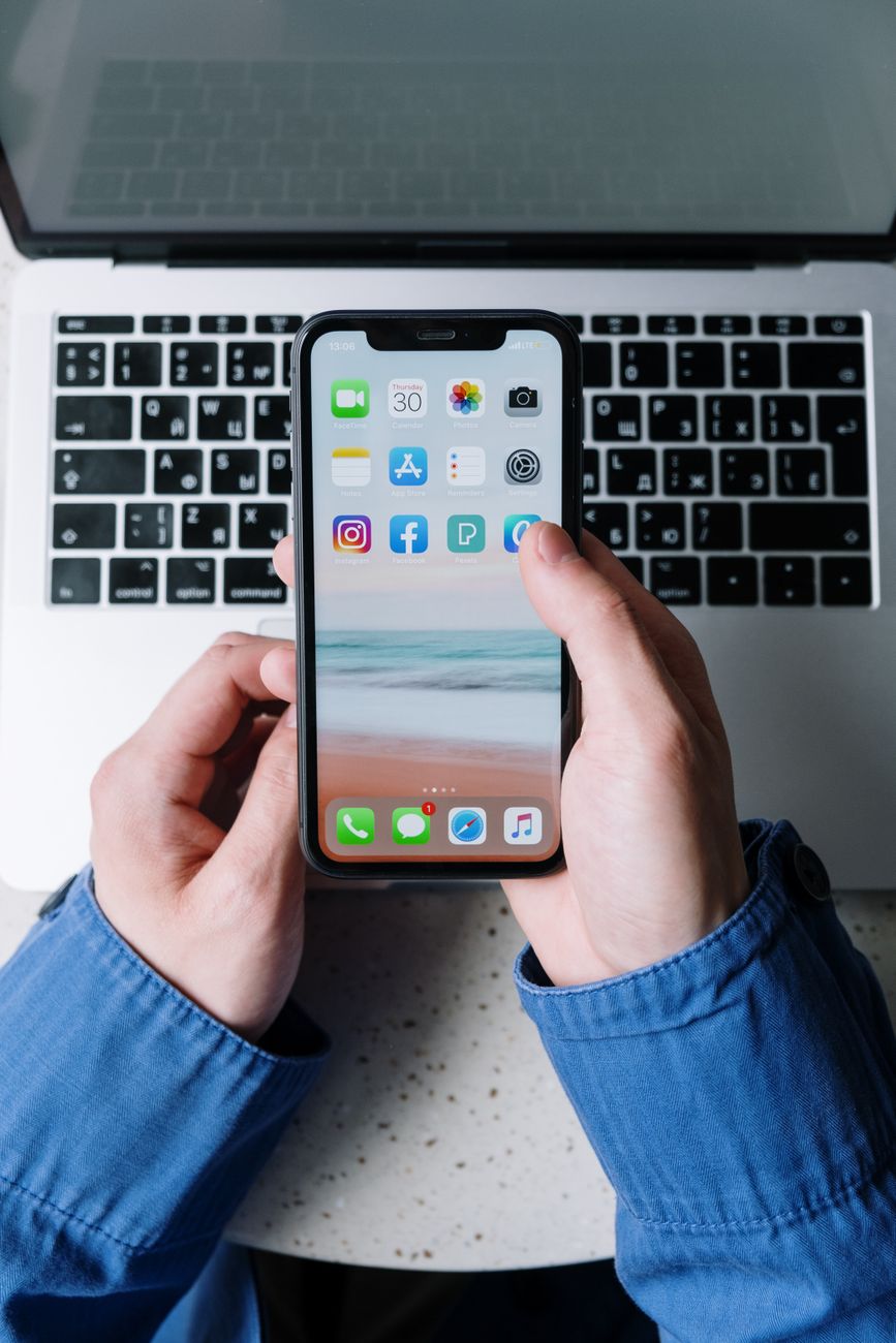 Vue rapprochée de mains tenant un smartphone avec des applications sur un clavier d'ordinateur portable.