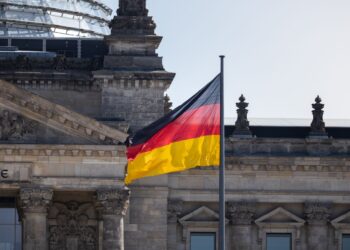 Le drapeau allemand flotte devant le célèbre bâtiment du Reichstag à Berlin, symbolisant la fierté nationale.