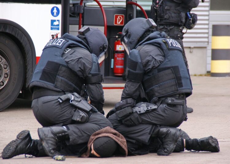 Des policiers allemands en tenue complète interpellent un suspect dans une zone urbaine à Hambourg.