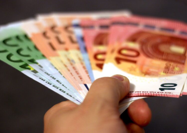 Gros plan d'une main tenant un éventail de billets en euros, symbolisant la richesse et l'échange de devises.