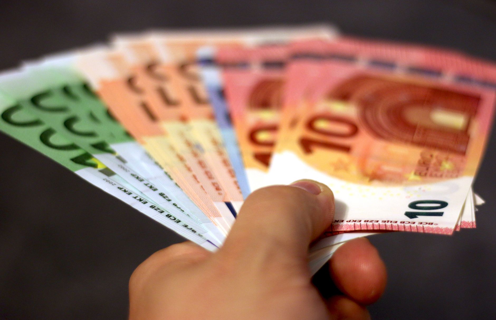 Gros plan d'une main tenant un éventail de billets en euros, symbolisant la richesse et l'échange de devises.