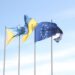 Les drapeaux de l'Union européenne et de l'Estonie flottent sous un ciel bleu dégagé, symbolisant l'unité et l'harmonie.