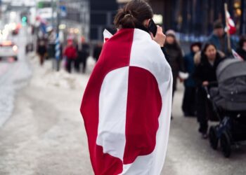 Une personne enveloppée dans un drapeau du Groenland prend des photos sur une rue enneigée à Nuuk, au Groenland.