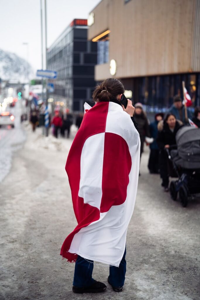 Une personne enveloppée dans un drapeau du Groenland prend des photos sur une rue enneigée à Nuuk, au Groenland.