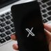 Une main tient un smartphone affichant une interface d'application moderne, avec un clavier d'ordinateur portable en arrière-plan.